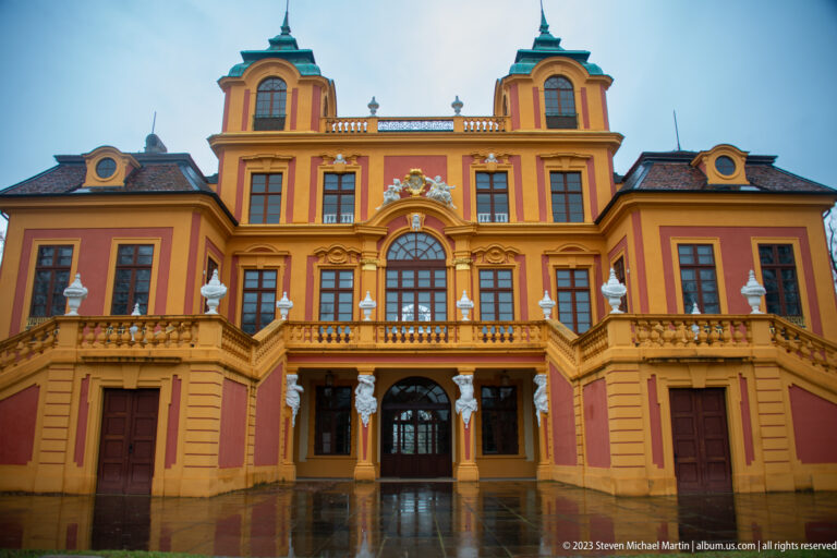 Straight-on view of Schloss Favorite central façade with terrace, arcade, twin roof towers, finials, and red-and-ocher walls.
