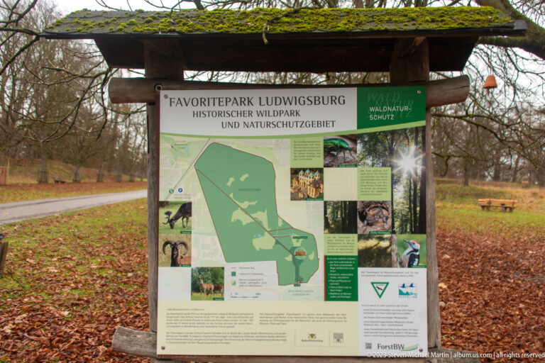 Favoritepark Ludwigsburg information board with map and photographs beneath a timber shelter in a wooded park.