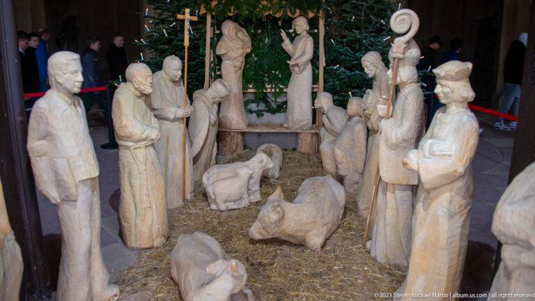 Wood-carved Nativity scene with Mary, Joseph, infant Jesus, shepherds, animals, and straw around a manger.
