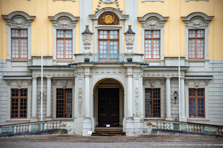 Ornate arched palace doorway with stone columns, relief carving, balcony, and tall windows on a yellow façade.