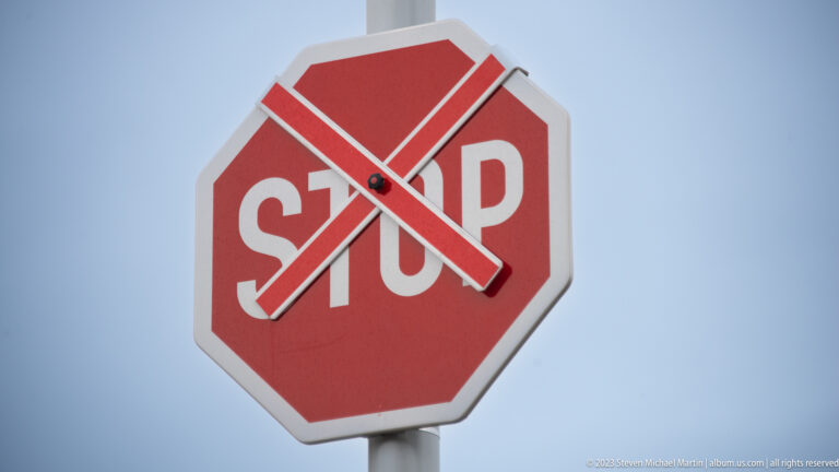 Red octagonal STOP sign converted into a clock with two white hands against a pale sky.