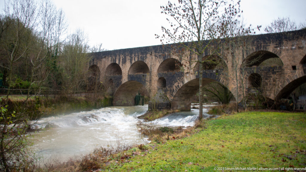 Two-tier stone Doppelbrücke crossing the fast-flowing Tauber River, with broad lower arches and a smaller upper arcade.
