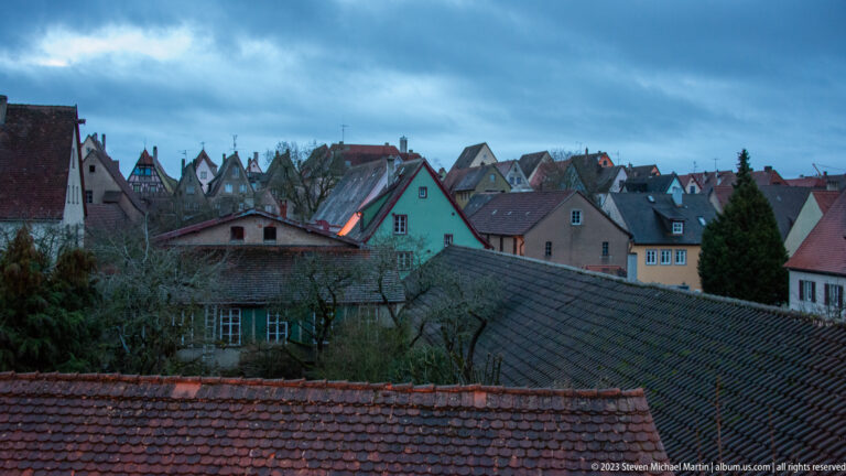 Elevated winter view over densely packed tiled roofs, colorful plaster houses, and scattered half-timbered gables in the old town.