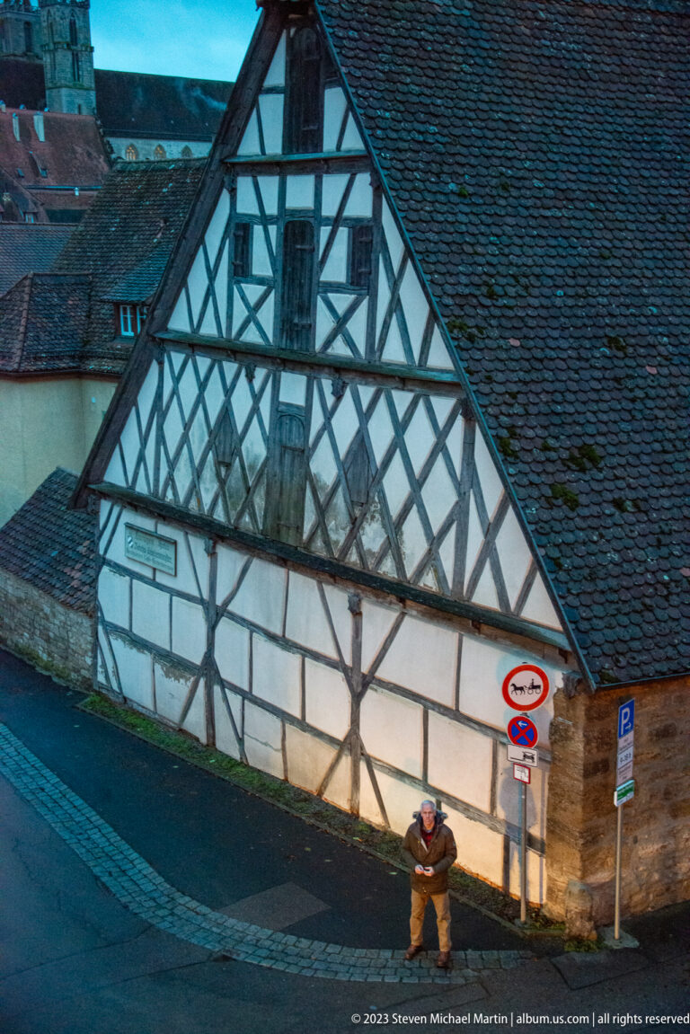 Large half-timbered gable with pale infill and weathered tile roof beside Rothenburg’s fortified edge at dusk.