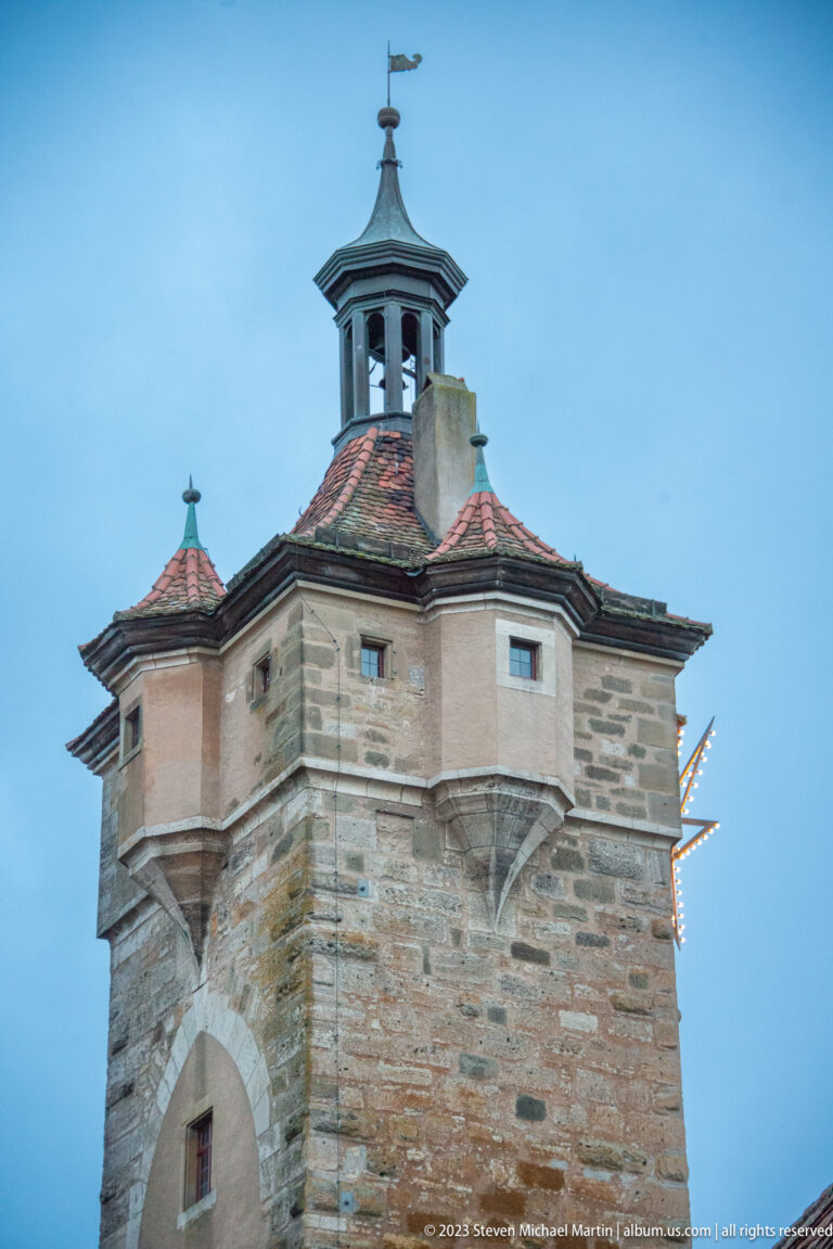 Massive stone defensive tower with broad arch, slit windows, tiled roof, and an open lantern-like cupola.
