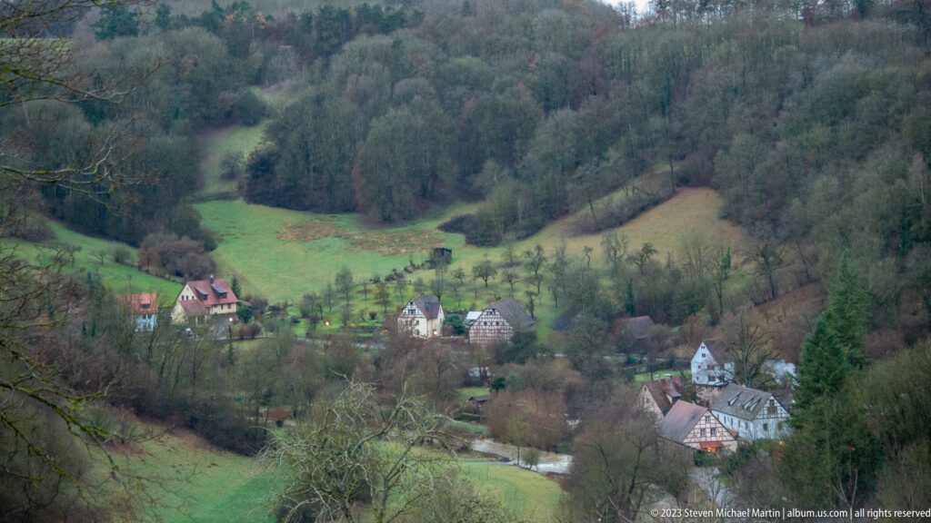 Elevated view of houses, green fields, orchards, roads, and wooded slopes in the Tauber valley below Rothenburg.