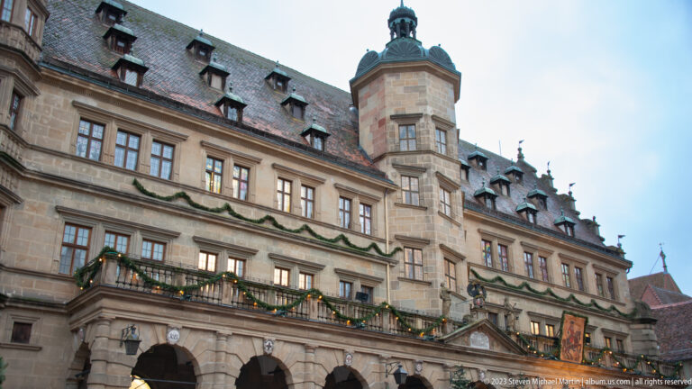 Renaissance Rothenburg Town Hall with arcaded ground floor, ordered windows, dormered roof, projecting polygonal tower, and Christmas garlands.
