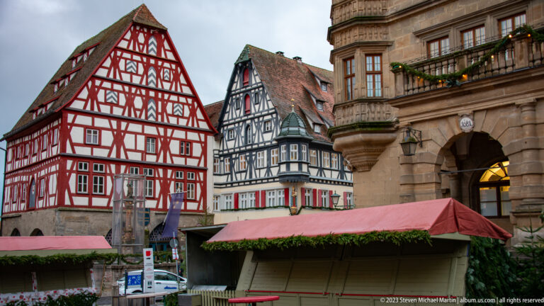 Red and dark half-timbered houses beside the stone Rathaus arcades, with closed Christmas-market stalls in the foreground.