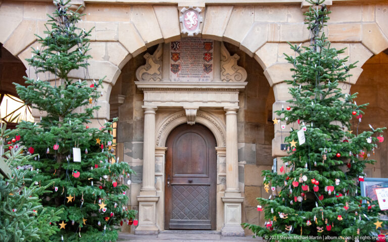 Ornate stone Rathaus doorway beneath a broad arch, flanked by two decorated Christmas trees and topped by heraldic panels.