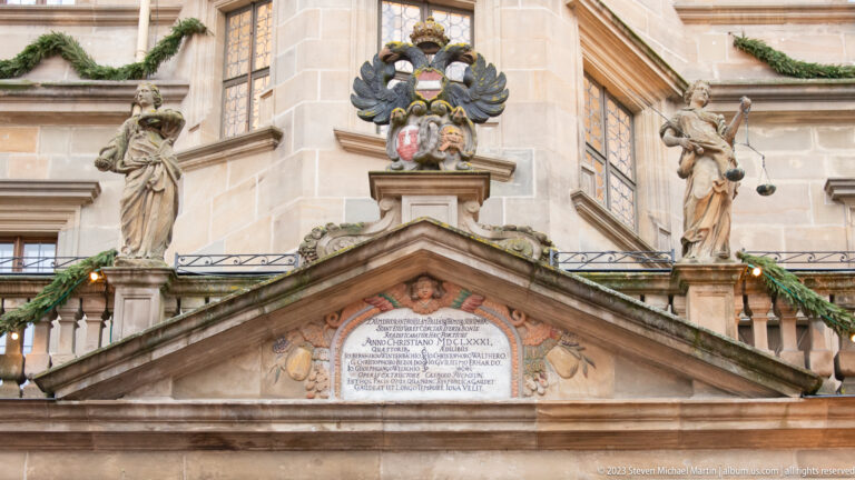 Rathaus pediment with inscription tablet, two standing statues, double-headed eagle, paired shields, and Christmas garlands.