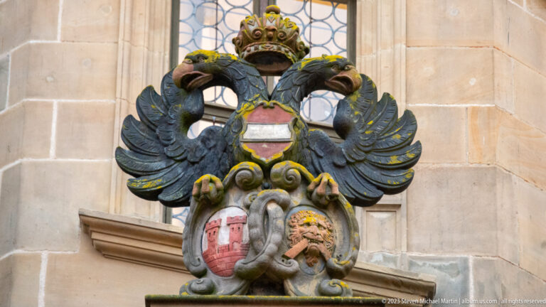 Crowned double-headed eagle above two shields and sculpted scrollwork on the pale stone Rathaus façade.