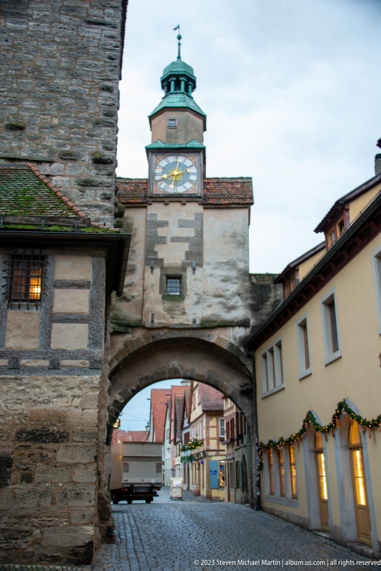 Markusturm with broad Röderbogen arch, large clock face, green-capped turret, and adjoining historic buildings viewed from the opposite side.