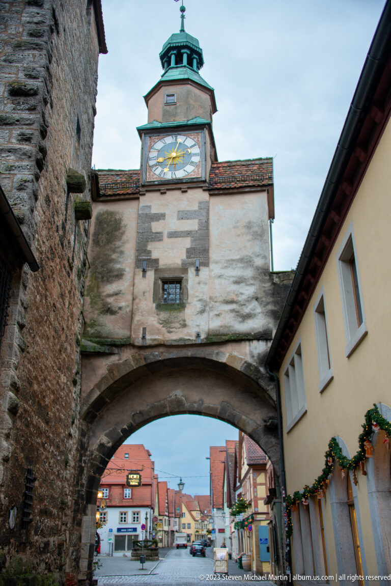 Centered view of Markusturm with large clock and Röderbogen arch framing colorful buildings beyond the gate.