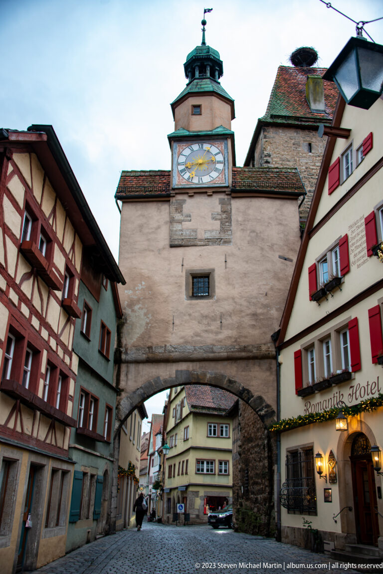 Markusturm and Röderbogen beside half-timbered houses and a building marked “Romantik Hotel” at a street junction.