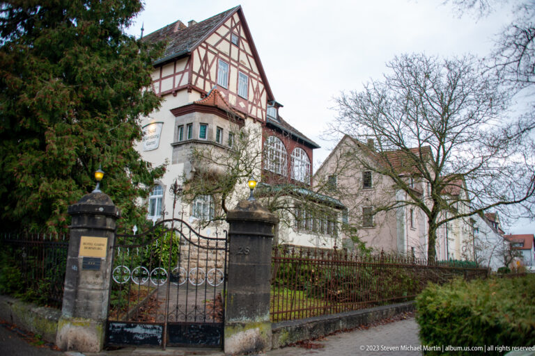 Large historic villa with half-timbered upper gable, glazed veranda, iron gate, stone posts, and winter garden.