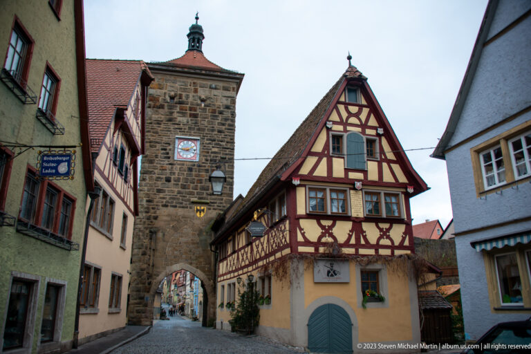Stone arched gate with heraldic plaque beside an ornate red-and-cream half-timbered gabled house.
