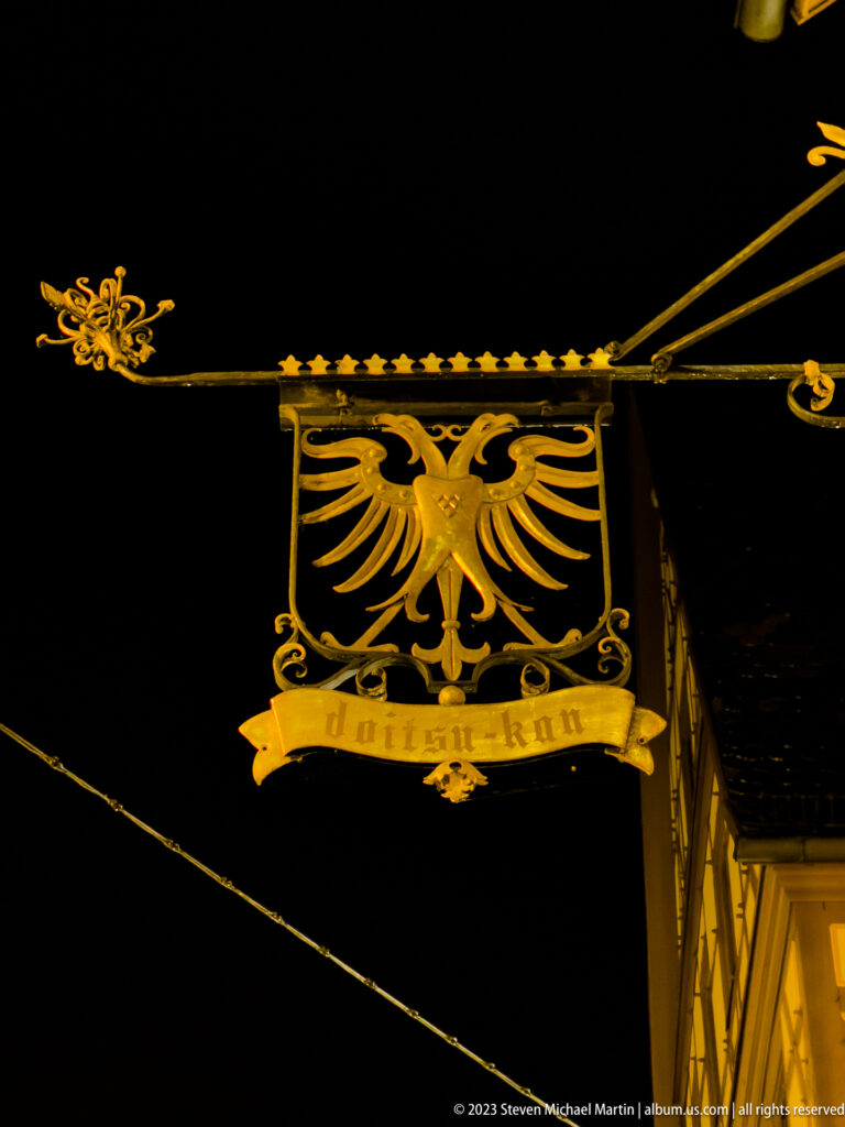 Golden double-headed eagle on an ornate wrought-iron projecting sign against a black night sky.