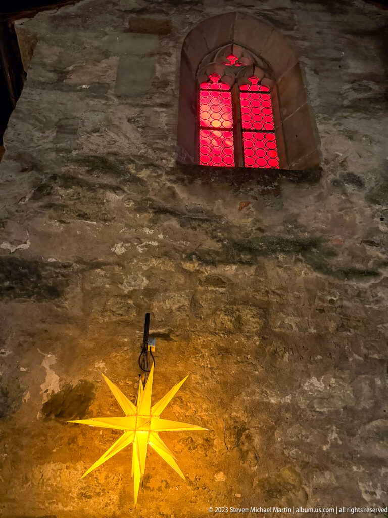 Glowing yellow star lantern below a small red-lit arched window set in rough historic stone masonry.