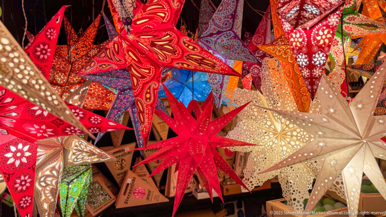 Dense display of red, white, orange, and patterned paper star lanterns with pierced surfaces and folded points.