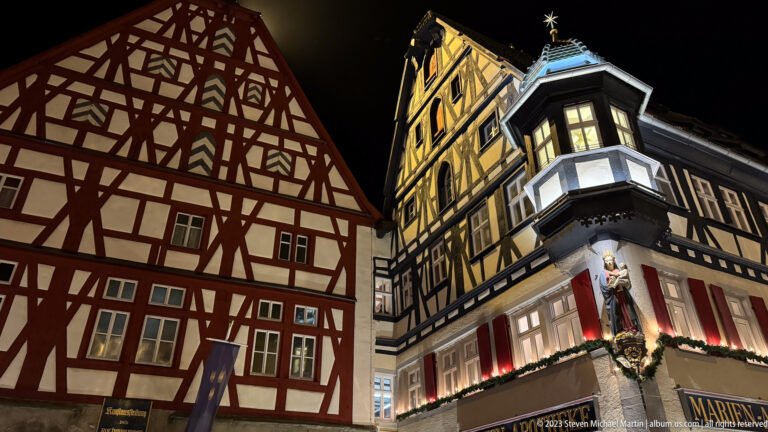 Two tall half-timbered buildings at night, one red-framed and one dark-framed with a projecting bay.