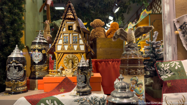 Display of decorated beer steins, miniature timber-framed clocks, carved figures, and other German souvenirs.