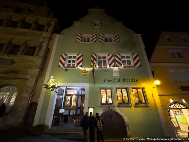 Gasthof Greifen façade with striped shutters, illuminated entrance, and small Christmas decorations at night.