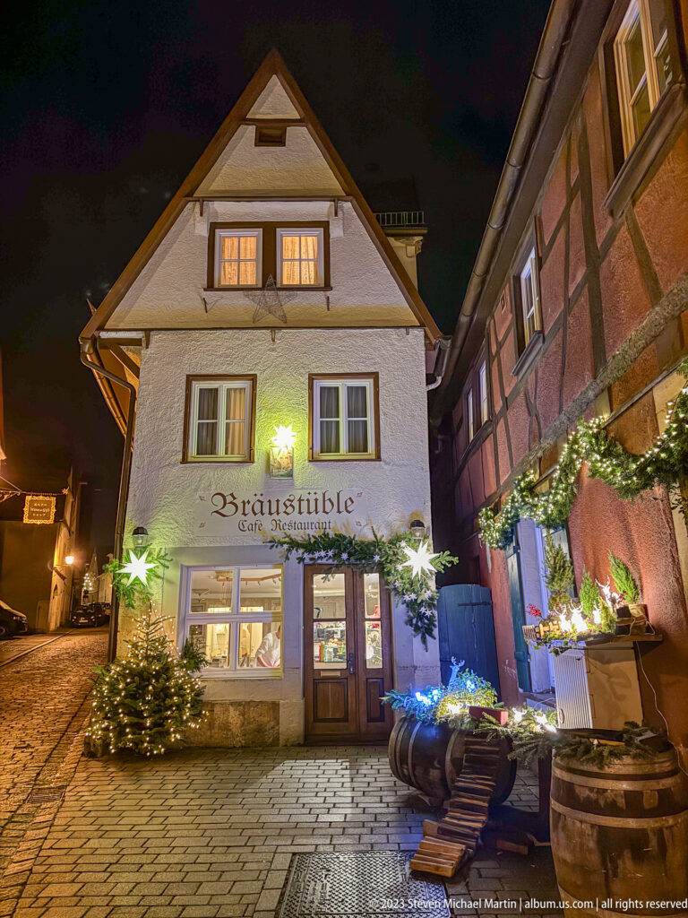 Bräustüble gabled façade on a wet cobblestone street beside a timber-framed building and Christmas decorations.