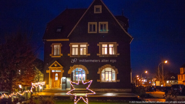 Front view of mittermeiers alter ego with steep gable, lit windows, and a large glowing star decoration outside.