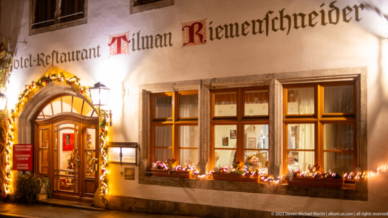 Hotel-Restaurant Tilman Riemenschneider façade with garlanded doorway, lit windows, and Christmas lights.