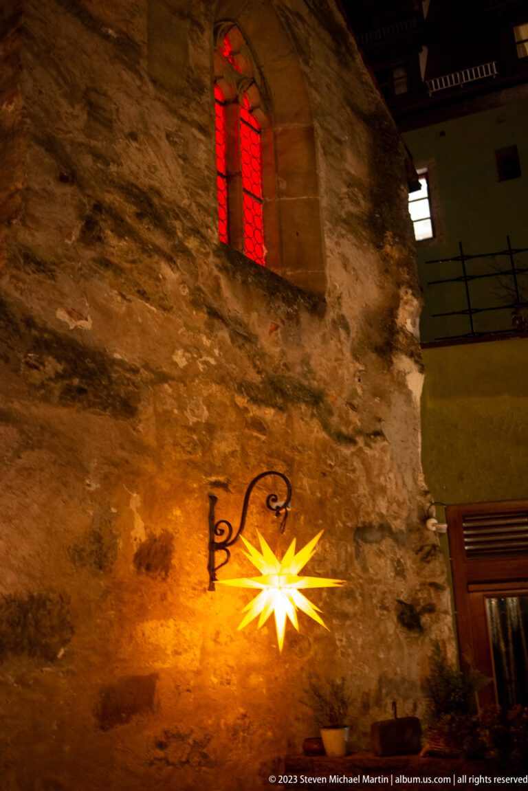 Glowing yellow star lamp on rough stone beneath a small red-lit window at night.