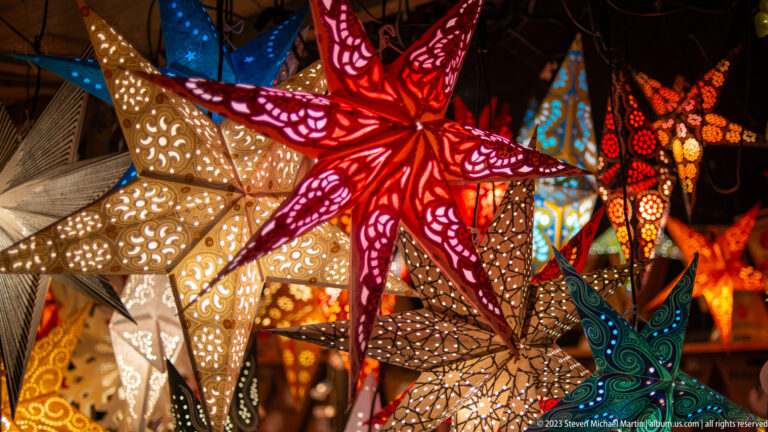Close display of red, white, turquoise, and patterned pierced-paper Christmas star lanterns.