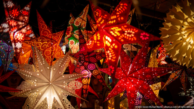 White star lantern surrounded by red, orange, green, and patterned illuminated paper stars in a dense display.