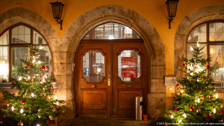 Wooden double doorway in a stone arch, centered between two decorated Christmas trees at Hotel Eisenhut.