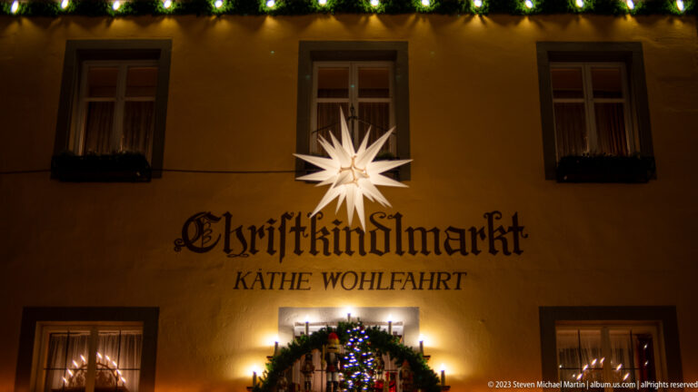 White Christmas star above “Christkindlmarkt Käthe Wohlfahrt” lettering on a decorated night façade.