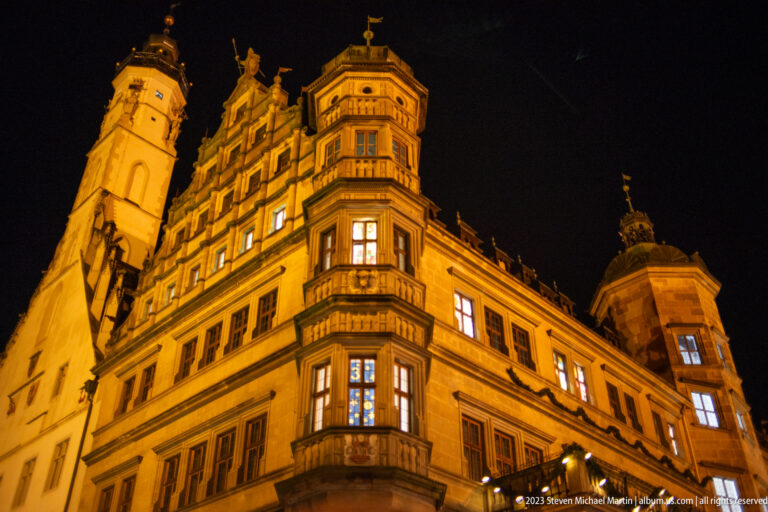Floodlit Renaissance Rathaus façade with corner oriel, rows of windows, decorative gables, and tower elements.