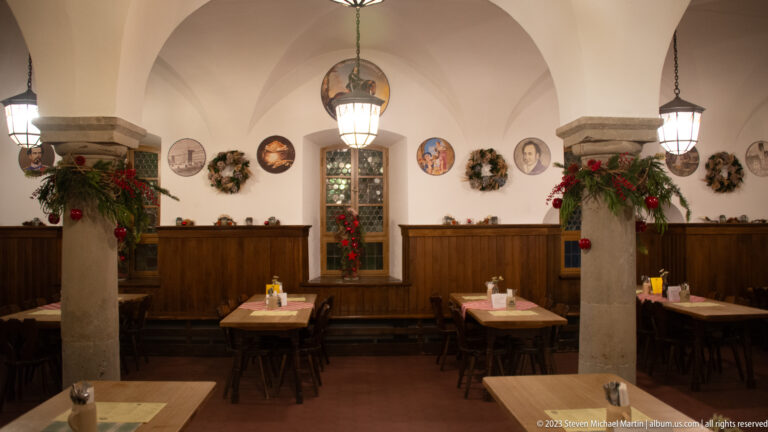 Dining room with white vaults, stone columns, wooden tables, wreaths, and red Christmas decorations.