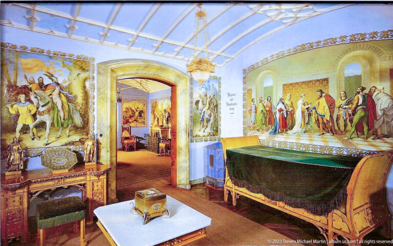 Carved bed with dark green covering beneath large historical murals in a richly furnished Hohenschwangau Castle room.