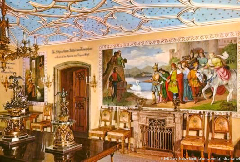 Large historical mural above carved high-backed chairs and ornate furnishings in Hohenschwangau Castle.
