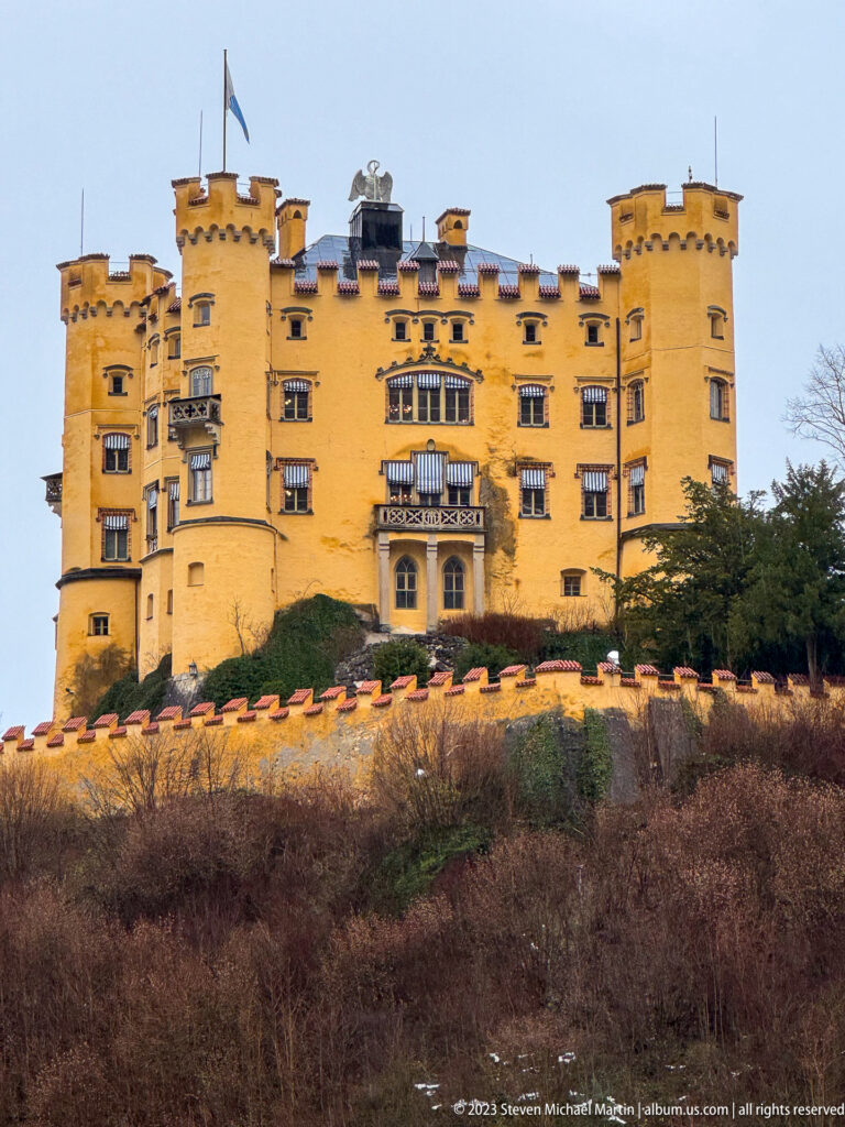 Close view of Hohenschwangau Castle with ochre walls, crenellated towers, balconies, and rows of windows.