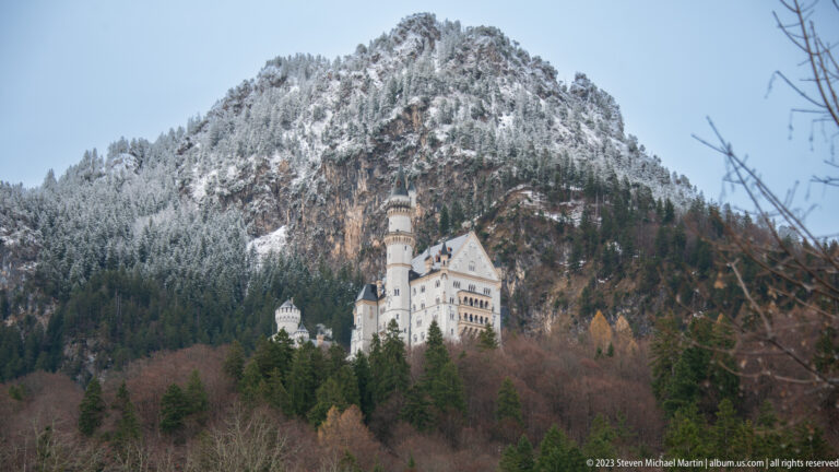Neuschwanstein Castle among winter trees beneath a steep, snow-dusted alpine mountain.
