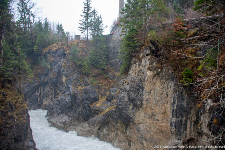 Fast river water passes through a narrow gorge between steep forested rock cliffs.