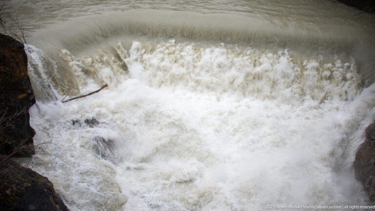 Foaming white river water surges over a low rocky drop in a close view.