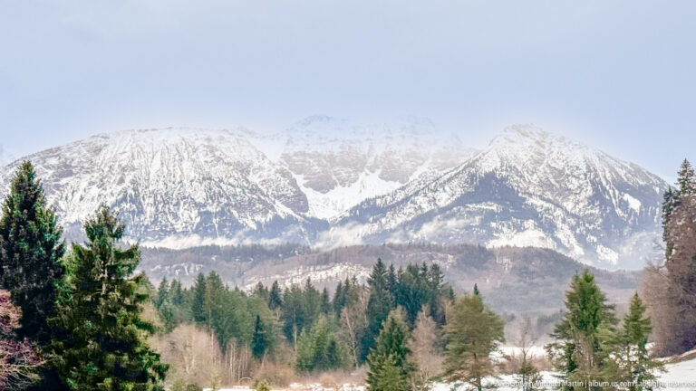Snow-covered mountain massif above evergreen trees and wintry foothills near Füssen.