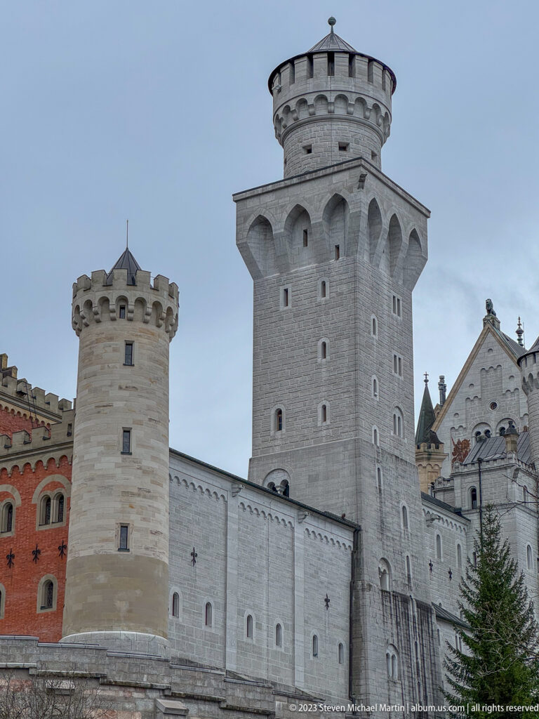 Tall pale square tower and smaller crenellated towers along Neuschwanstein’s western wall.
