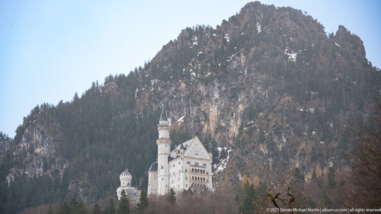Neuschwanstein Castle appears beneath a large forested and rocky mountain slope.