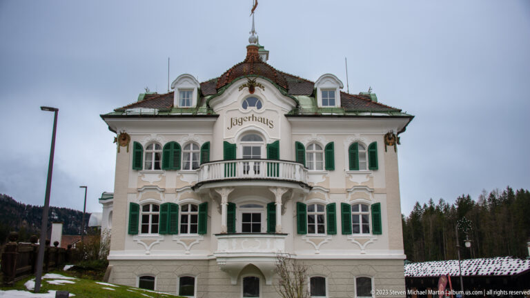 White Jägerhaus villa with green shutters, central balcony, curved gables, and decorative roof crest.