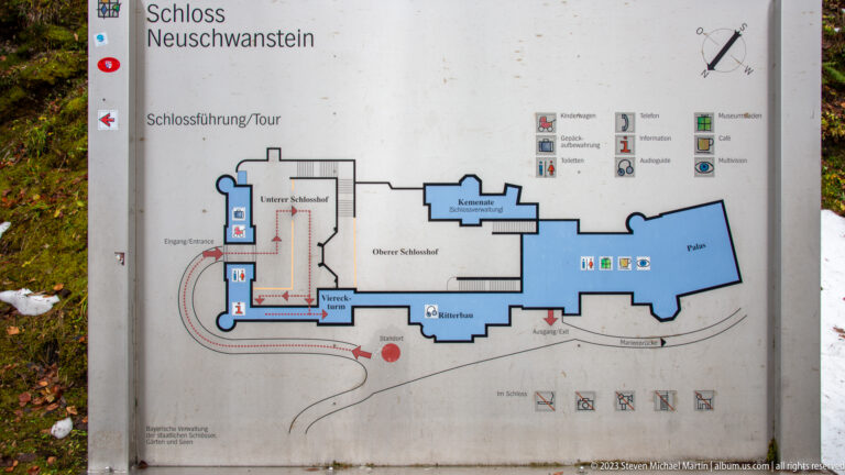 Posted Neuschwanstein Castle tour map showing a floor plan, room blocks, route arrows, and visitor symbols.