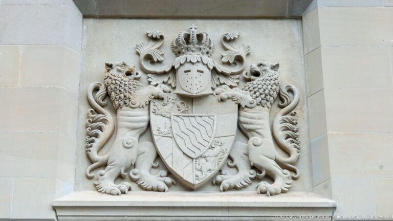Carved stone coat of arms with quartered shield, crowned helmet, two rampant lions, and ornate mantling.