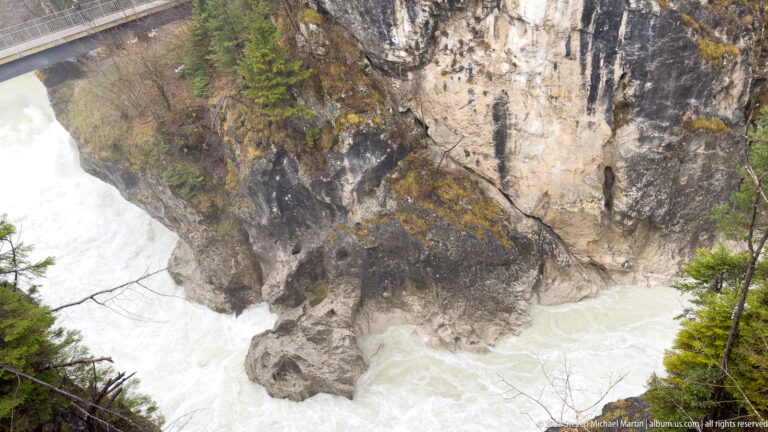 Sheer weathered rock wall above churning pale-green river water in a narrow gorge.