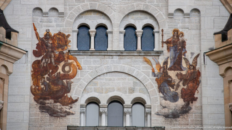 Painted armored and robed figures beside arched windows on the pale stone Palas façade at Neuschwanstein Castle.